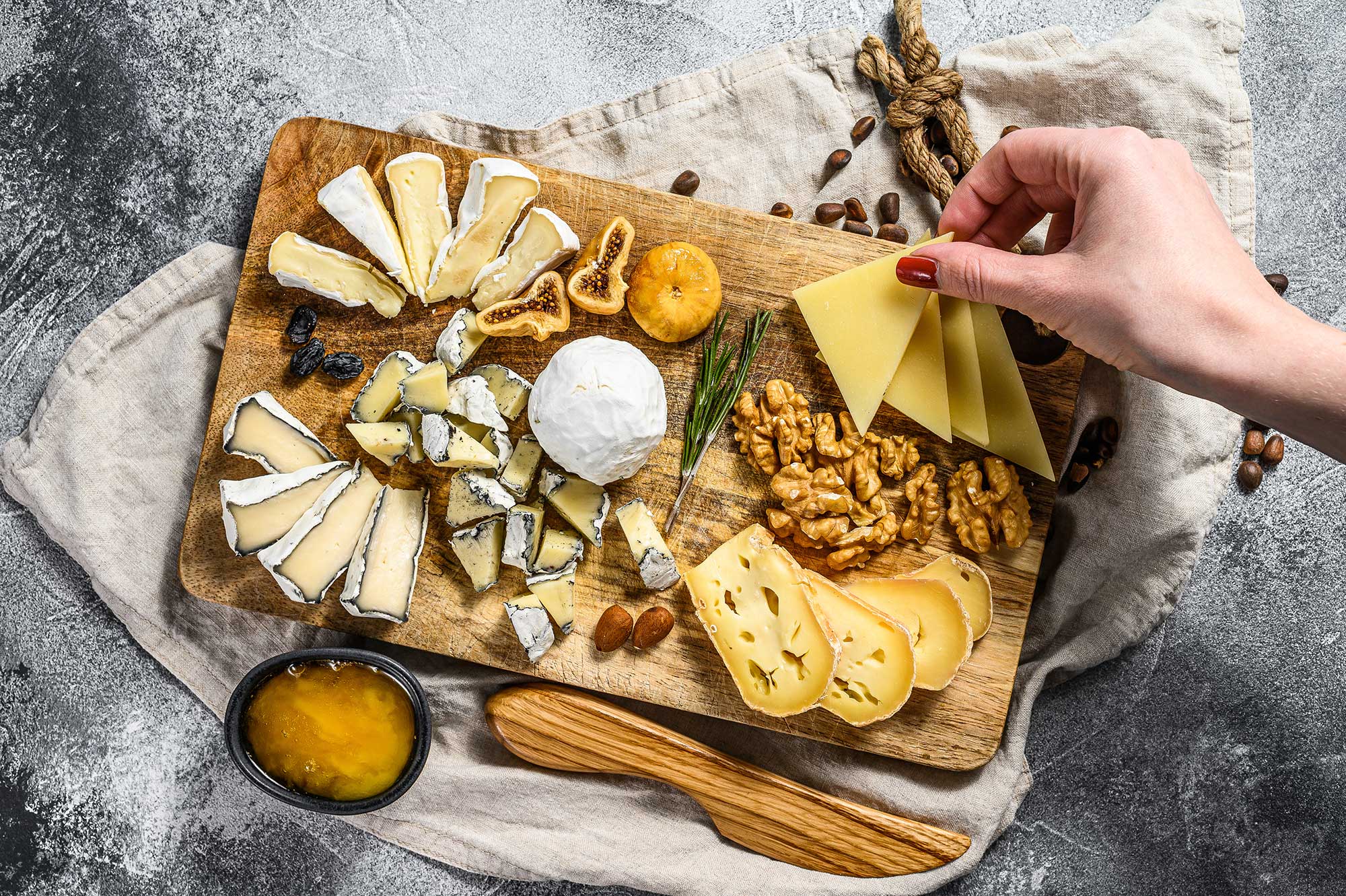 hand takes a piece of cheese from cheese plate served with nuts and figs