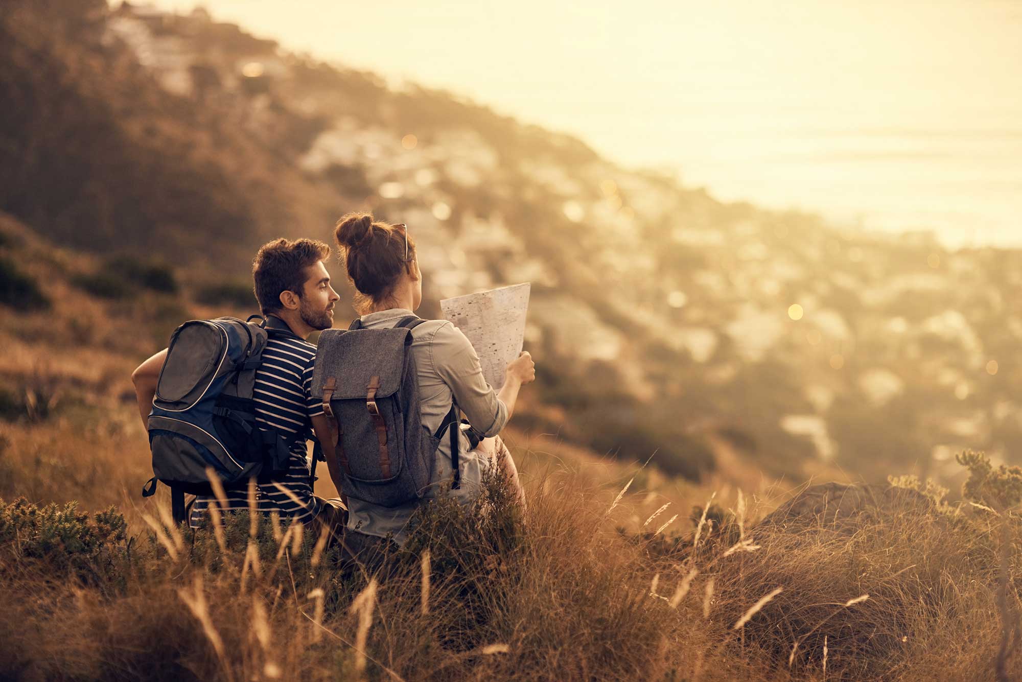 rearview shot of a couple looking at a map while taking a break from hiking